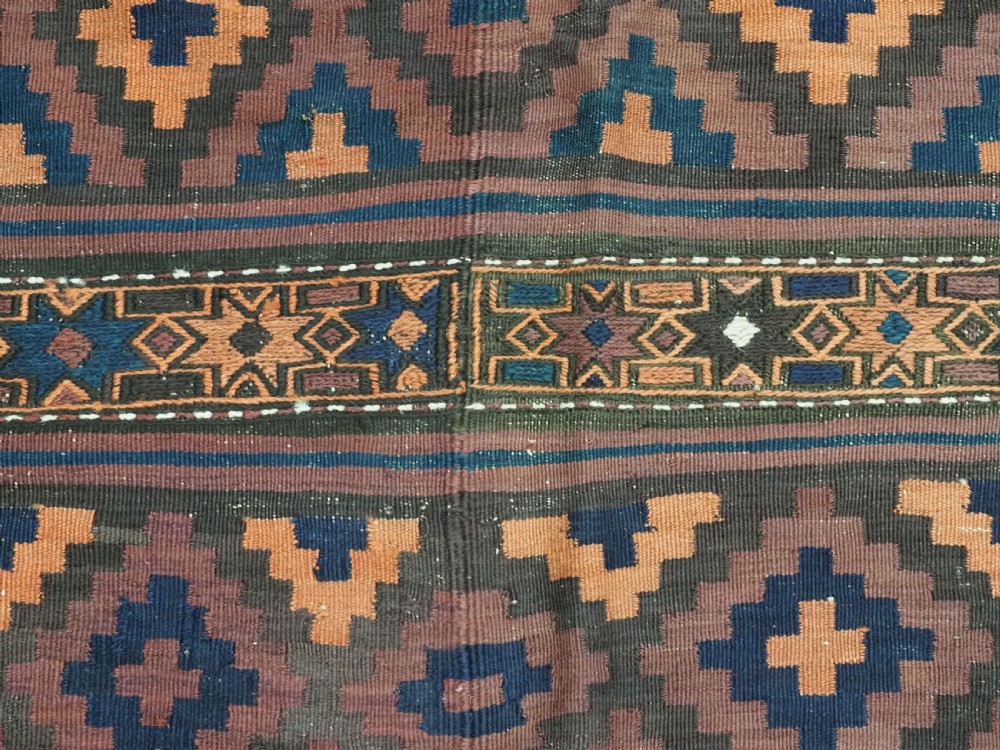 A large flatweave Baluch wool kilim rug featuring two joined panels with geometric diamond bands in terracotta, indigo, and dark brown hues. View XII