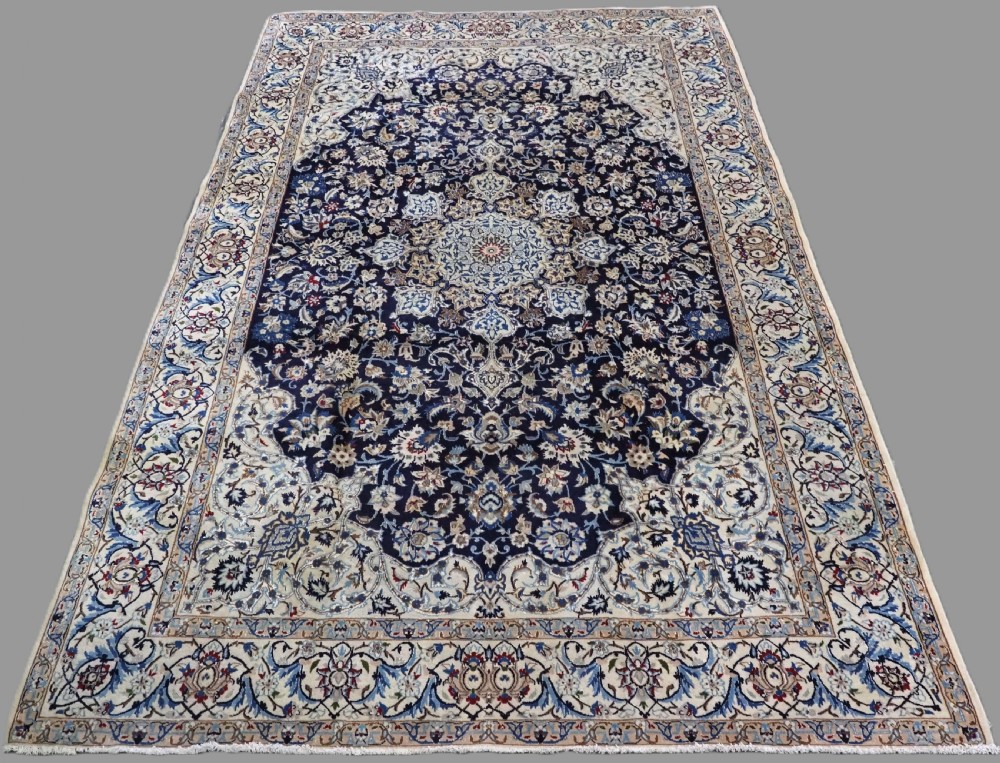 An antique hand-knotted Persian Nain carpet featuring an intricate central medallion in light blue and cream set against a deep navy blue field surrounded by elaborate floral borders.