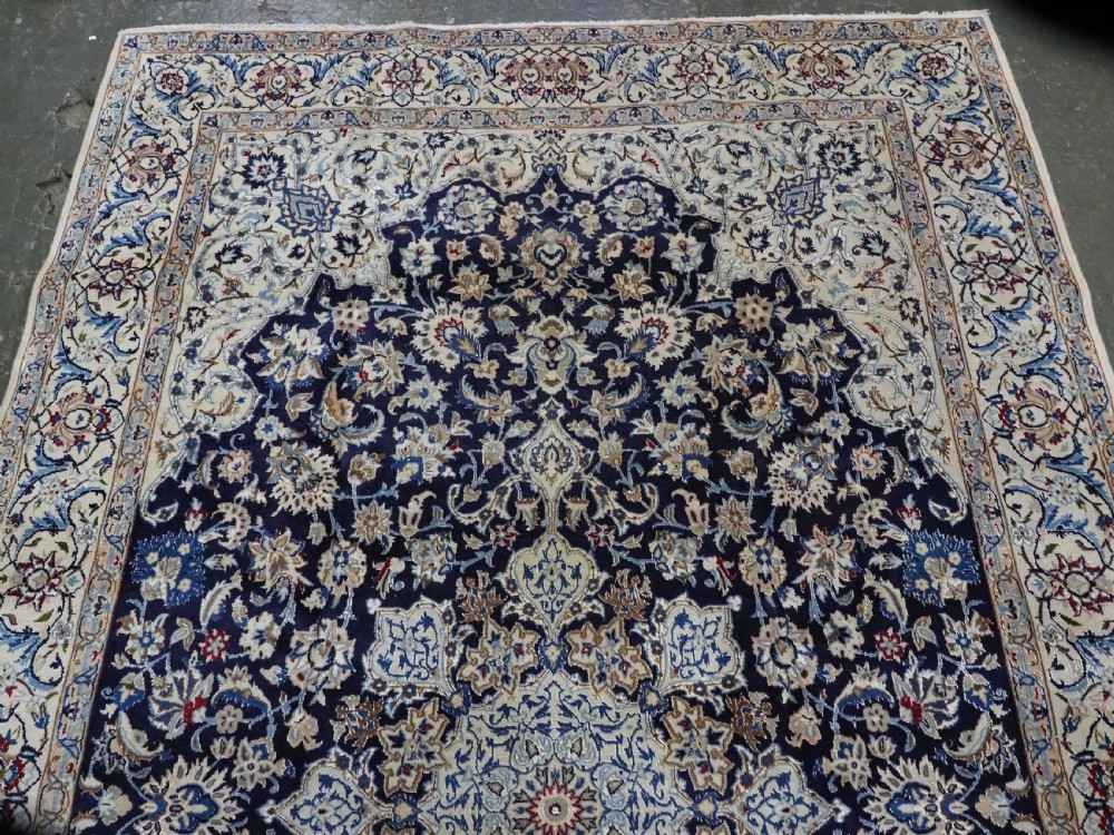 An antique hand-knotted Persian Nain carpet featuring an intricate central medallion in light blue and cream set against a deep navy blue field surrounded by elaborate floral borders. View III