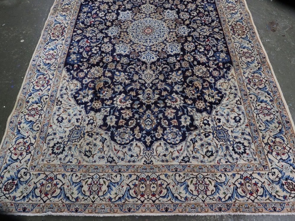 An antique hand-knotted Persian Nain carpet featuring an intricate central medallion in light blue and cream set against a deep navy blue field surrounded by elaborate floral borders. View V