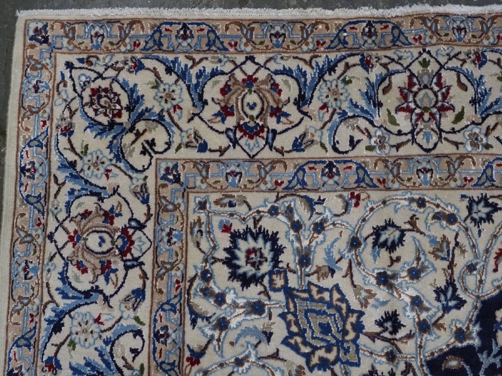 An antique hand-knotted Persian Nain carpet featuring an intricate central medallion in light blue and cream set against a deep navy blue field surrounded by elaborate floral borders. View VI