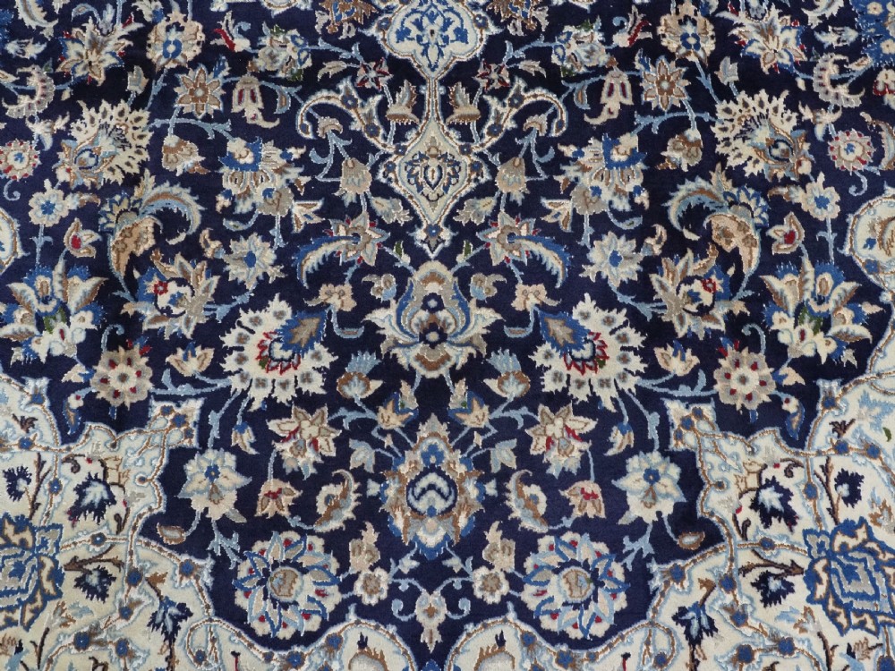 An antique hand-knotted Persian Nain carpet featuring an intricate central medallion in light blue and cream set against a deep navy blue field surrounded by elaborate floral borders. View X