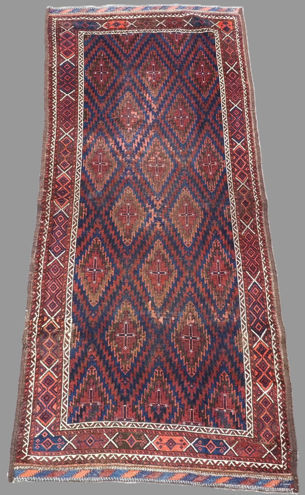 An antique hand-woven Arab Baluch runner rug featuring a dark navy blue and deep red geometric diamond lattice pattern with outer geometric borders.