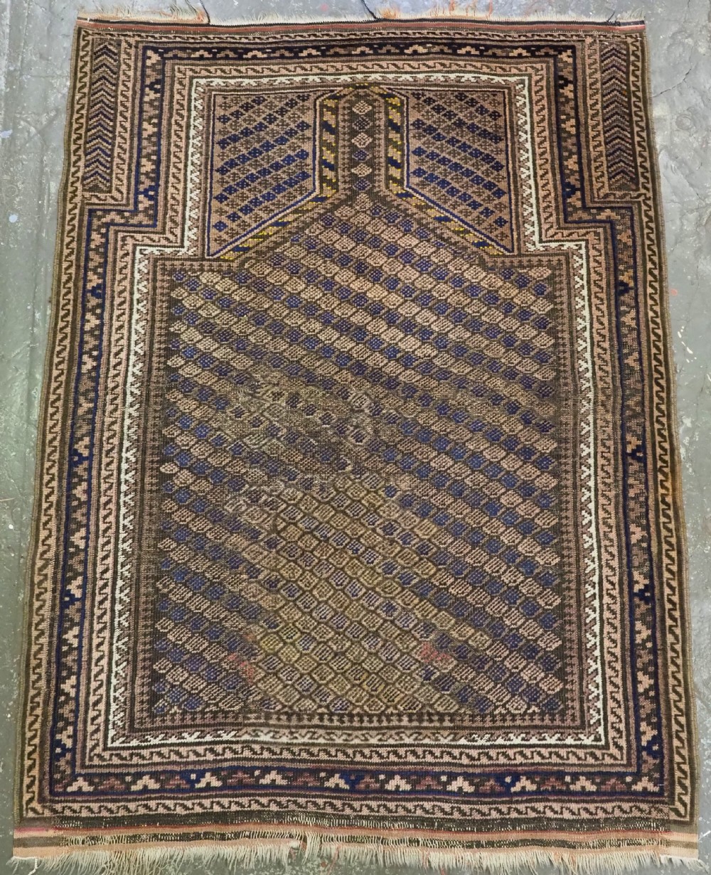 An antique hand-woven Baluch prayer rug featuring a dark brown and indigo geometric diamond lattice pattern framed within a arched mihrab niche.