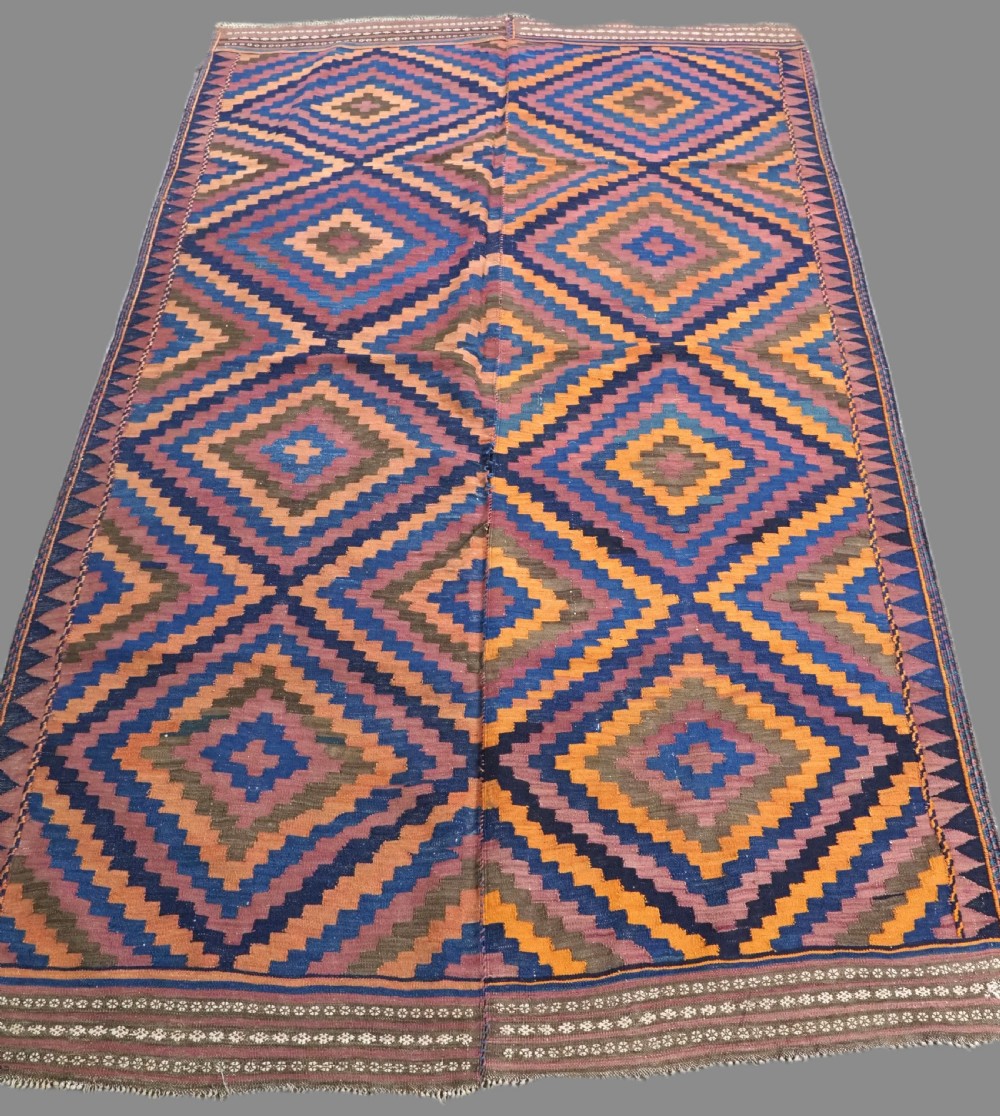An antique flatwoven wool Baluch kilim with repeating geometric diamond patterns in blue, orange, brown, and purple shades, constructed in two joined panels.