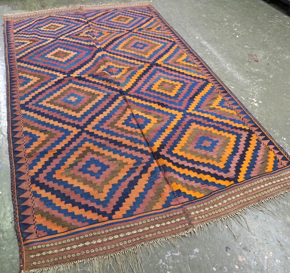 An antique flatwoven wool Baluch kilim with repeating geometric diamond patterns in blue, orange, brown, and purple shades, constructed in two joined panels. View II