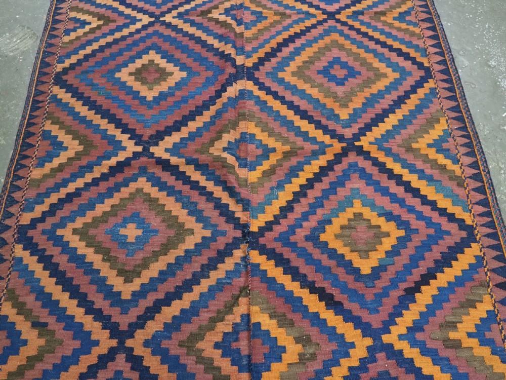 An antique flatwoven wool Baluch kilim with repeating geometric diamond patterns in blue, orange, brown, and purple shades, constructed in two joined panels. View III