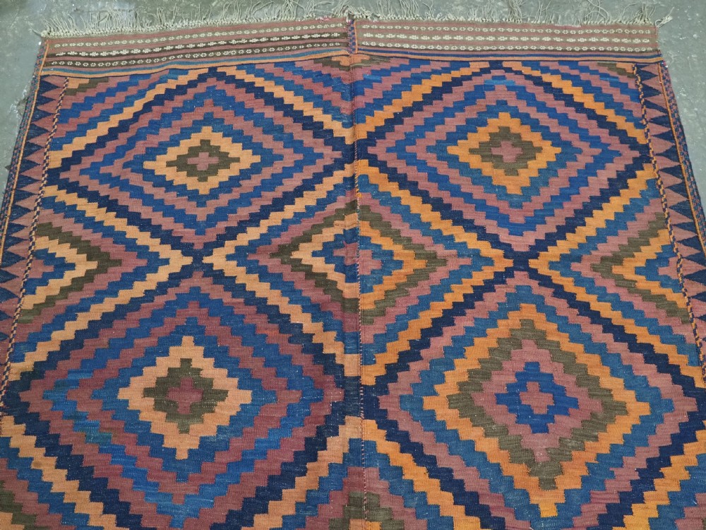 An antique flatwoven wool Baluch kilim with repeating geometric diamond patterns in blue, orange, brown, and purple shades, constructed in two joined panels. View V