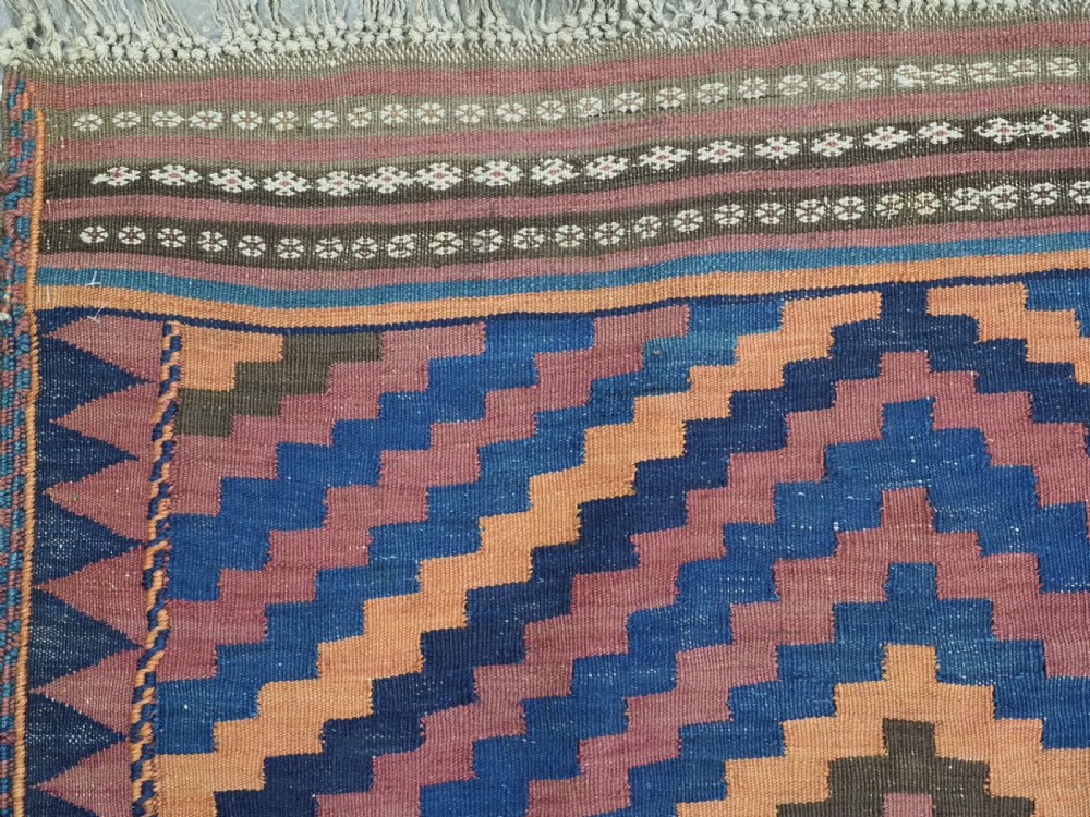 An antique flatwoven wool Baluch kilim with repeating geometric diamond patterns in blue, orange, brown, and purple shades, constructed in two joined panels. View VI