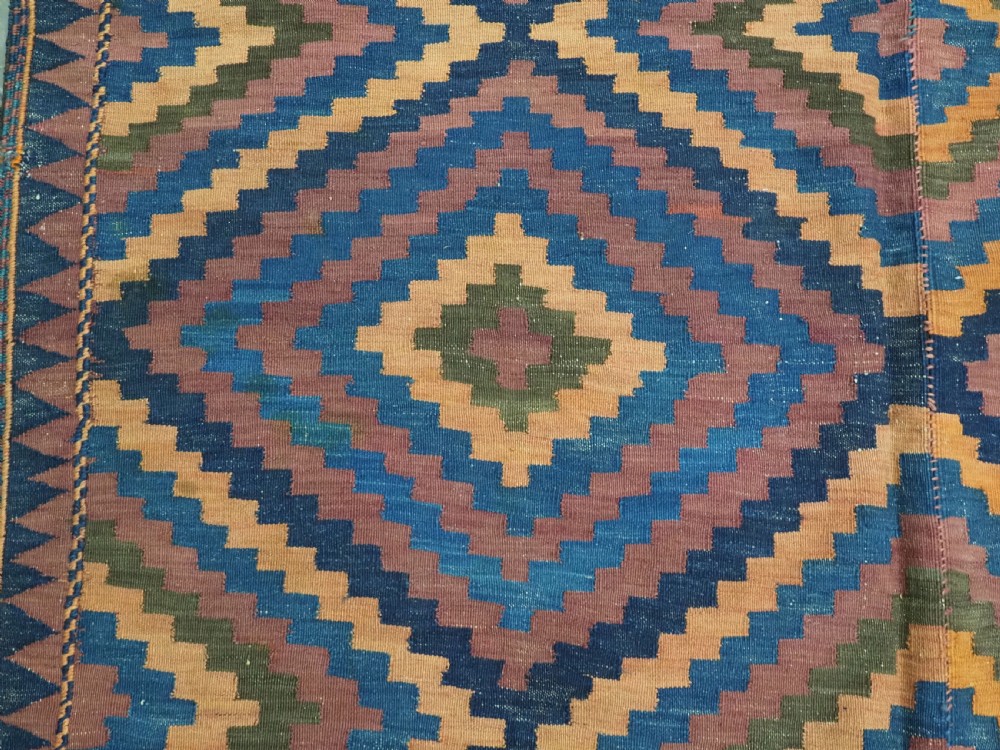An antique flatwoven wool Baluch kilim with repeating geometric diamond patterns in blue, orange, brown, and purple shades, constructed in two joined panels. View X