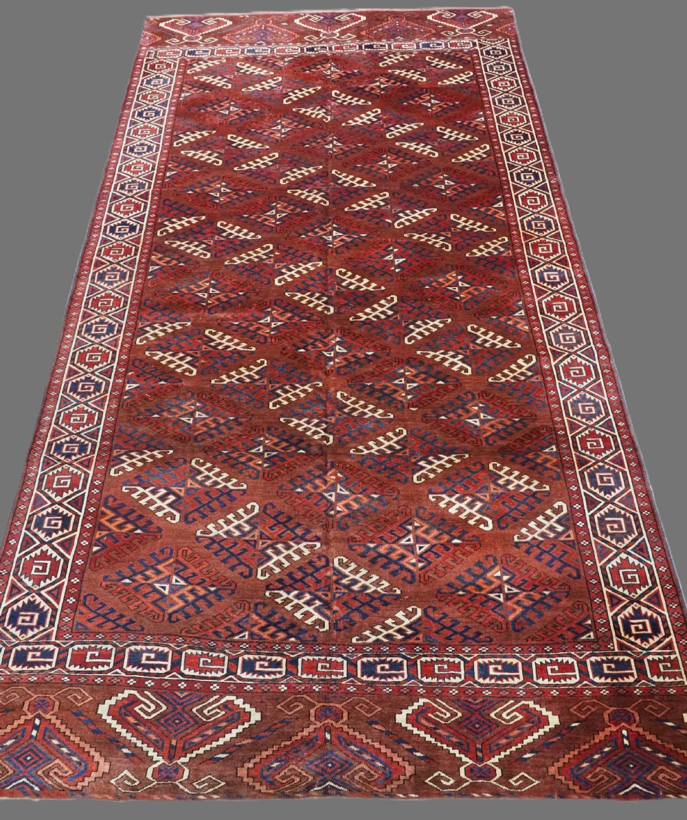 A long hand-knotted antique wool rug featuring a repeating dyrnak gul pattern in deep red, navy, and ivory tones surrounded by geometric borders.