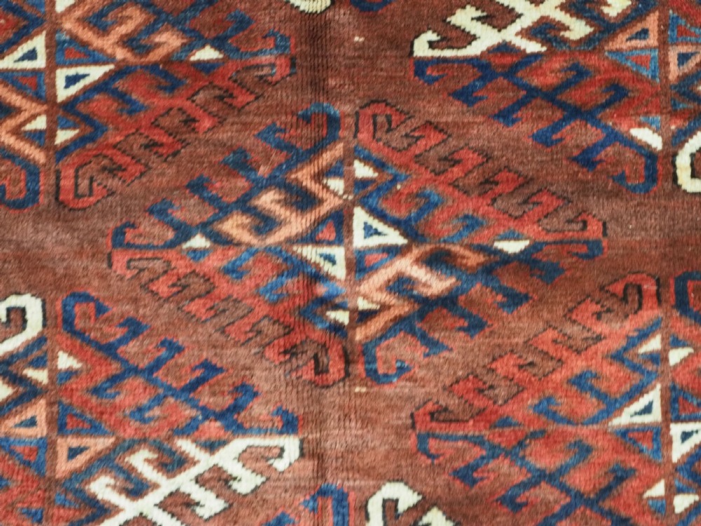 A long hand-knotted antique wool rug featuring a repeating dyrnak gul pattern in deep red, navy, and ivory tones surrounded by geometric borders. View X