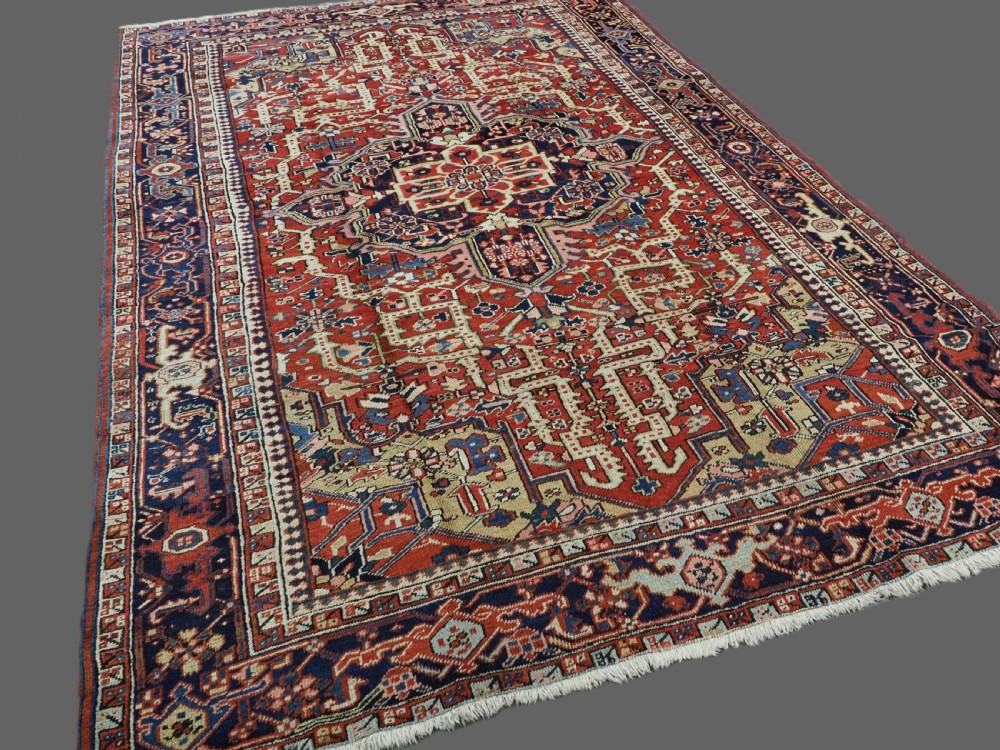 An antique Persian Heriz wool carpet featuring a central geometric medallion, stylized floral motifs in red, blue, and cream, framed by a complex multi-tiered border. View II