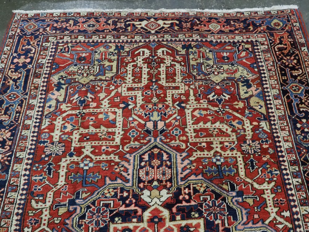 An antique Persian Heriz wool carpet featuring a central geometric medallion, stylized floral motifs in red, blue, and cream, framed by a complex multi-tiered border. View III