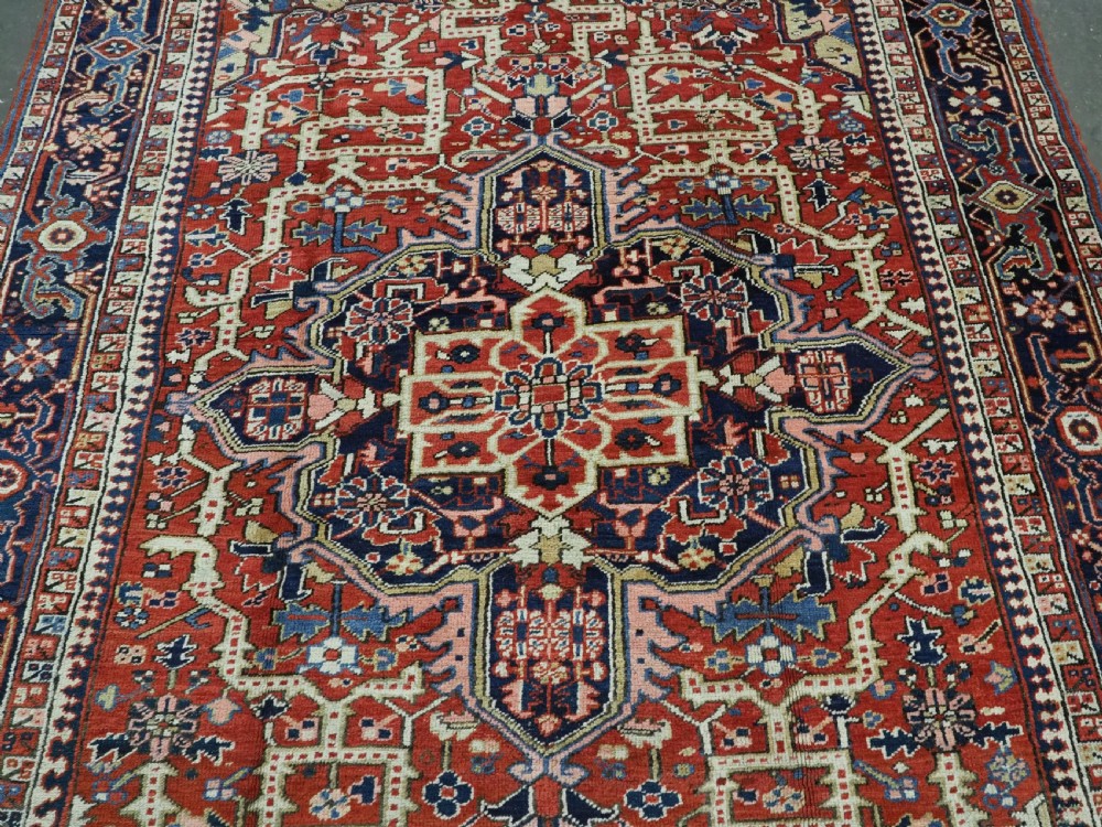 An antique Persian Heriz wool carpet featuring a central geometric medallion, stylized floral motifs in red, blue, and cream, framed by a complex multi-tiered border. View IV