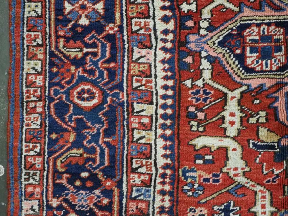 An antique Persian Heriz wool carpet featuring a central geometric medallion, stylized floral motifs in red, blue, and cream, framed by a complex multi-tiered border. View VII