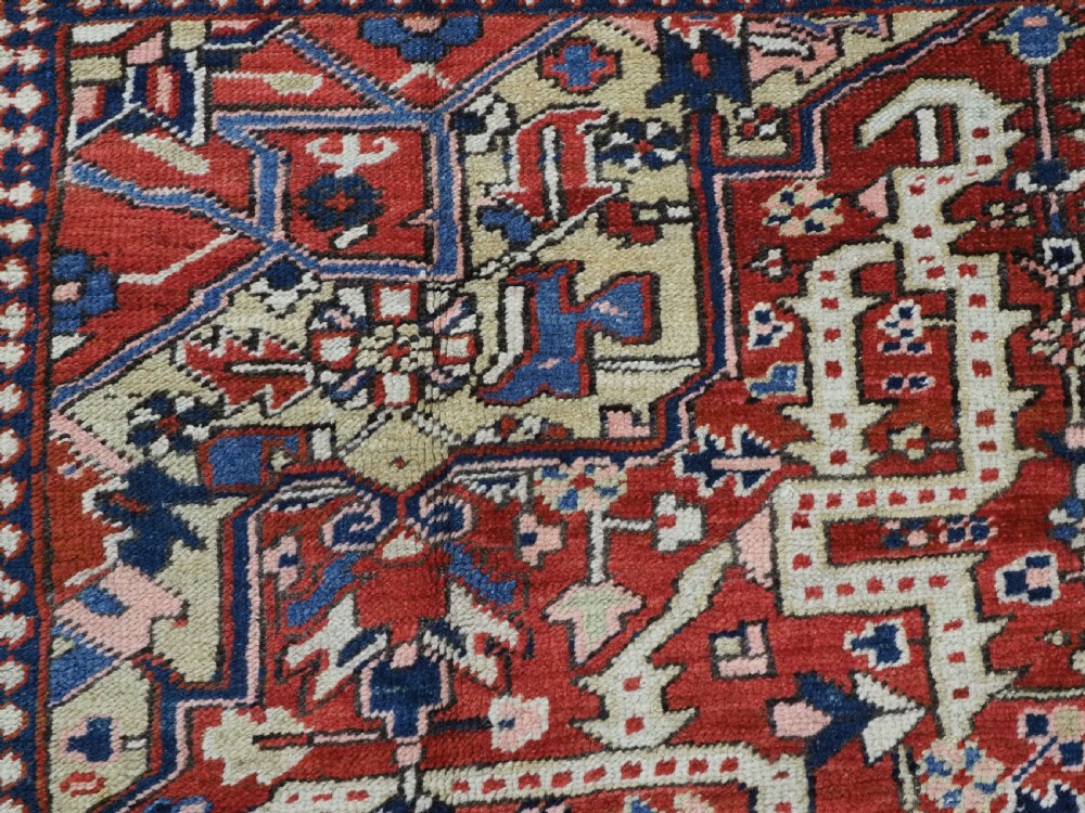 An antique Persian Heriz wool carpet featuring a central geometric medallion, stylized floral motifs in red, blue, and cream, framed by a complex multi-tiered border. View VIII