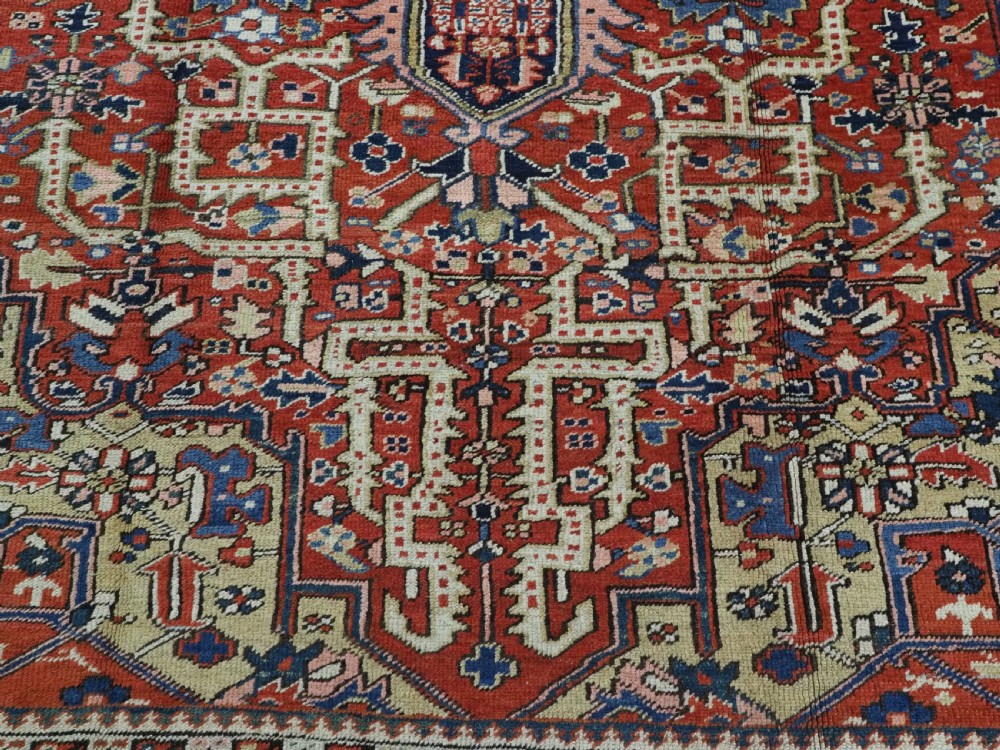 An antique Persian Heriz wool carpet featuring a central geometric medallion, stylized floral motifs in red, blue, and cream, framed by a complex multi-tiered border. View XI