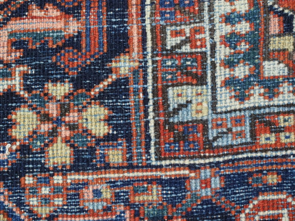 An antique Persian Heriz wool carpet featuring a central geometric medallion, stylized floral motifs in red, blue, and cream, framed by a complex multi-tiered border. View XIV