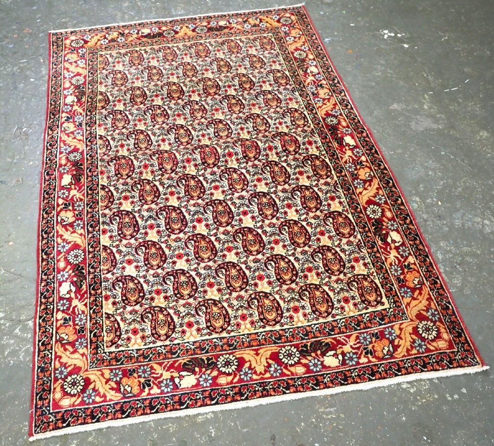 An antique Kirman rug featuring a repeat floral boteh pattern on a cream field enclosed by a detailed red and cream floral border. View II