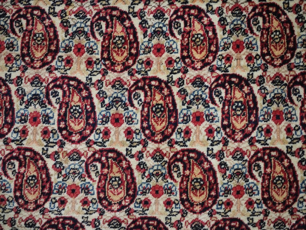 An antique Kirman rug featuring a repeat floral boteh pattern on a cream field enclosed by a detailed red and cream floral border. View IX