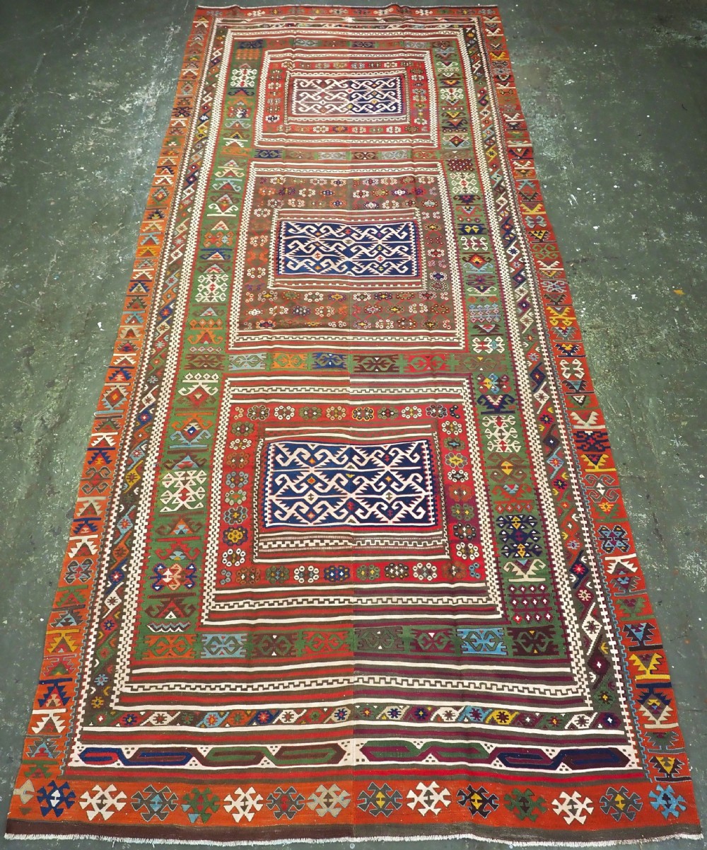 An antique Turkish Reyhanli flatweave kilim runner featuring multi-coloured geometric medallions joined along a central seam with a red border.