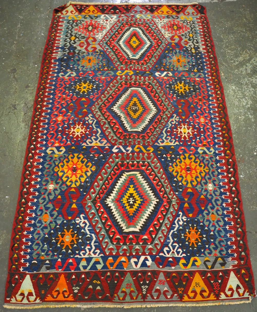 A handwoven Turkish Esme kilim rug displaying geometric diamond medallions in red, blue, yellow, and green wool.