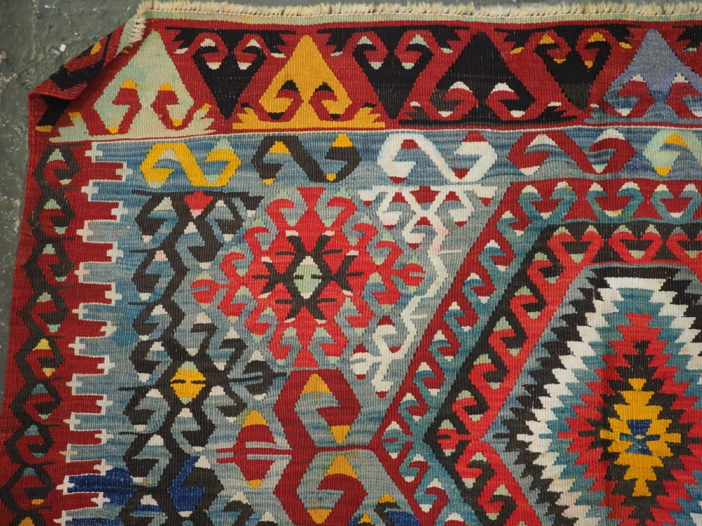 A handwoven Turkish Esme kilim rug displaying geometric diamond medallions in red, blue, yellow, and green wool. View V