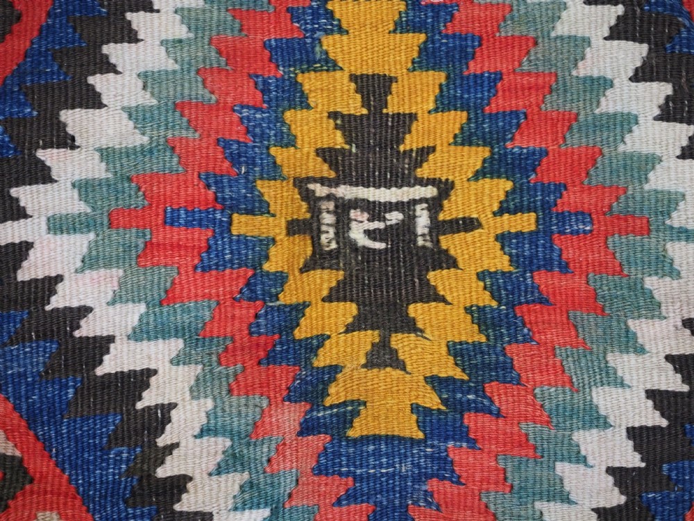 A handwoven Turkish Esme kilim rug displaying geometric diamond medallions in red, blue, yellow, and green wool. View X