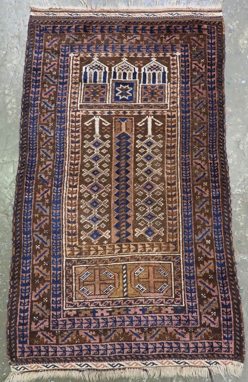 An antique Afghan Sistan Baluch hand-knotted wool prayer rug featuring a dark brown geometric field with a stylized mihrab arch motif and patterned borders.