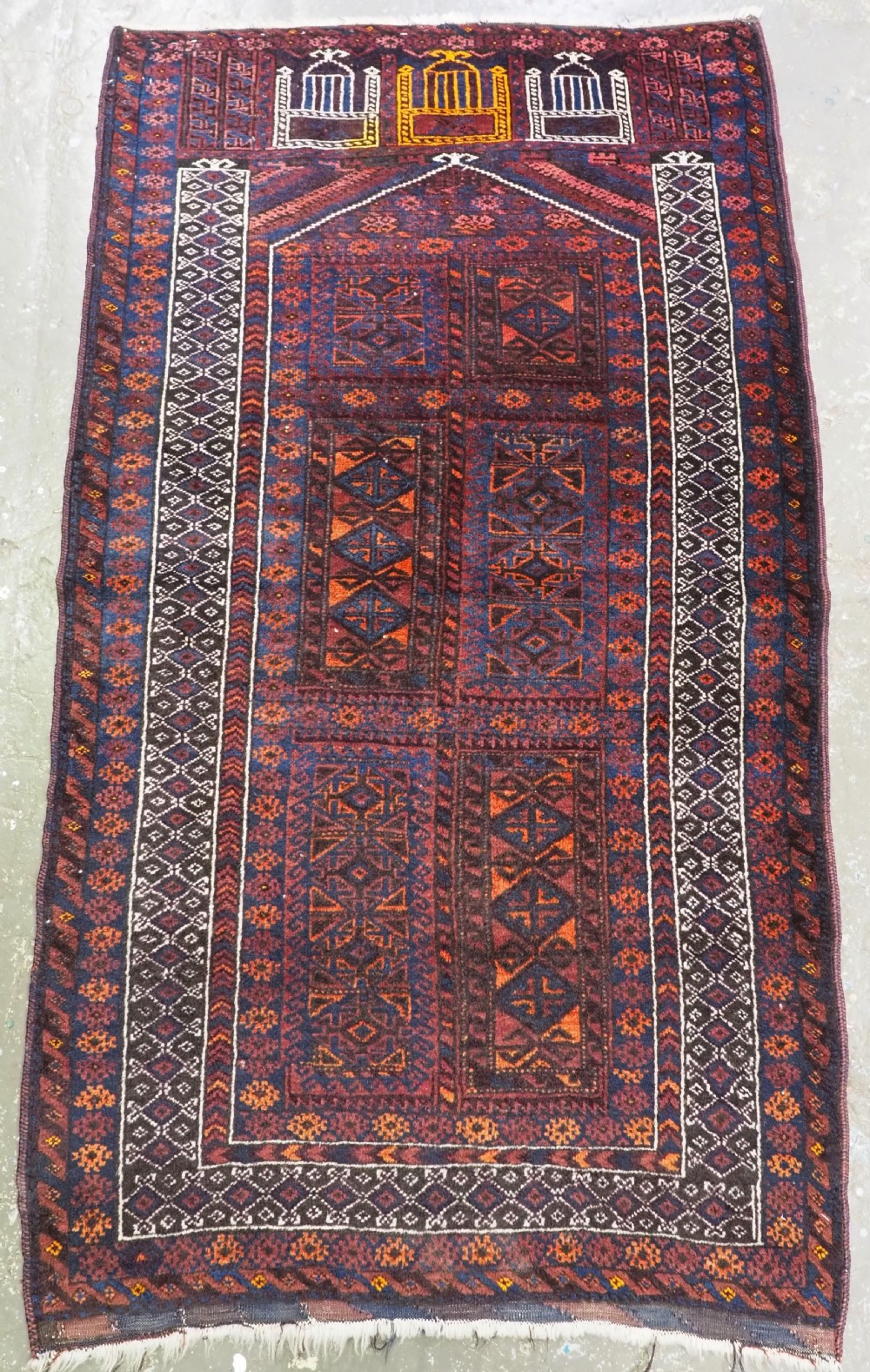 An antique Afghan Baluch hand-knotted wool prayer rug featuring a triple arch seh mihrab motif and dark red, navy, and orange geometric patterns.
