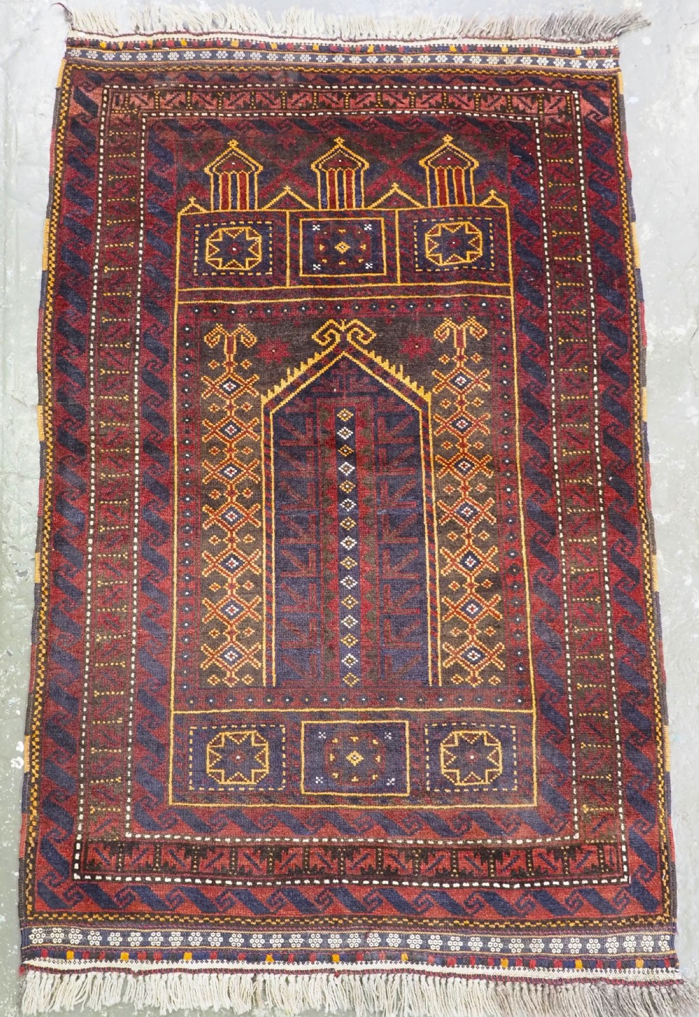 An antique handwoven Afghan wool prayer rug featuring three geometric arch motifs in deep red, navy, ochre, and dark brown hues.