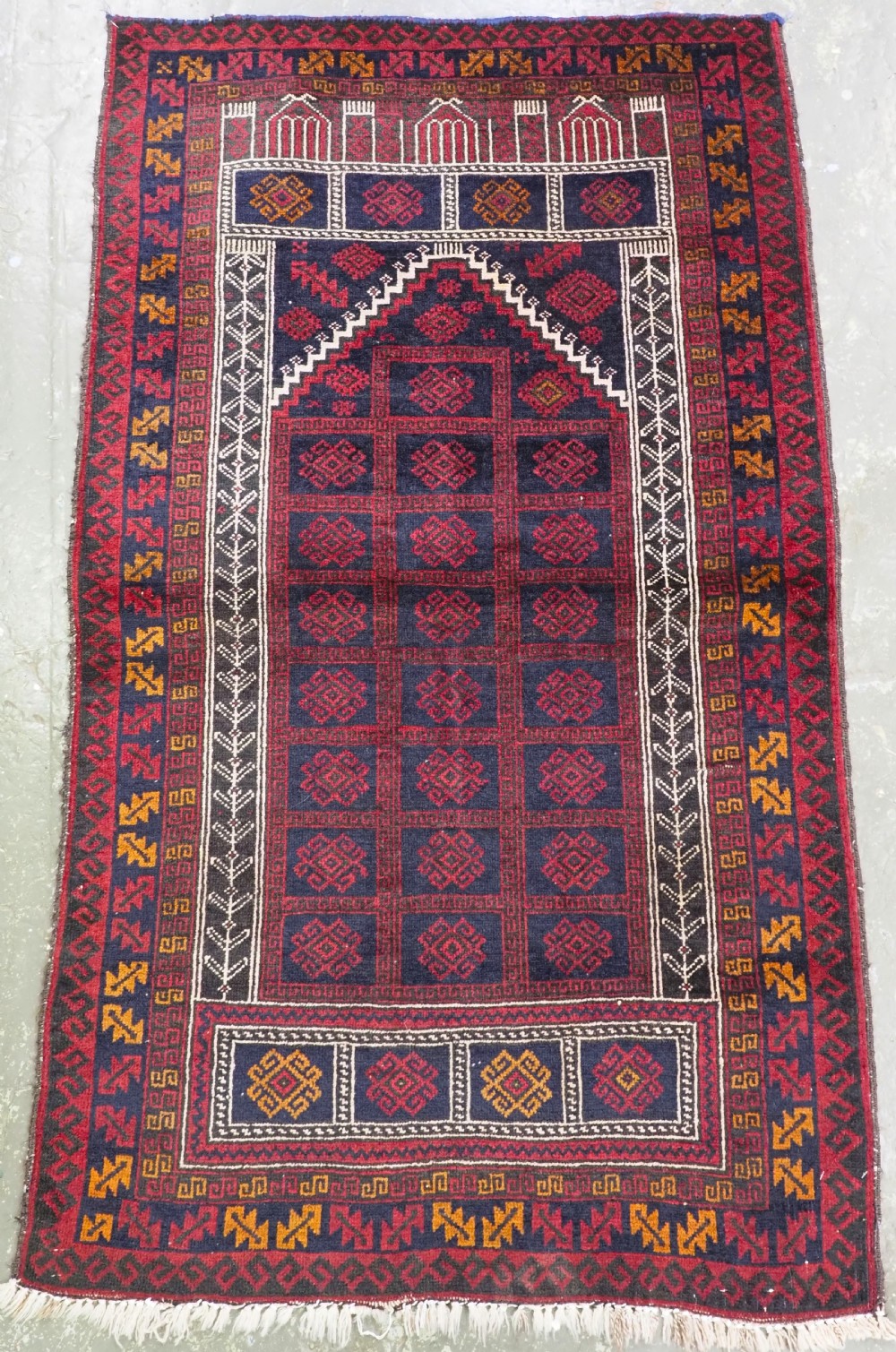 An antique hand-knotted wool Afghan prayer rug featuring a triple mihrab design in dark red, navy blue, and yellow geometric patterns.