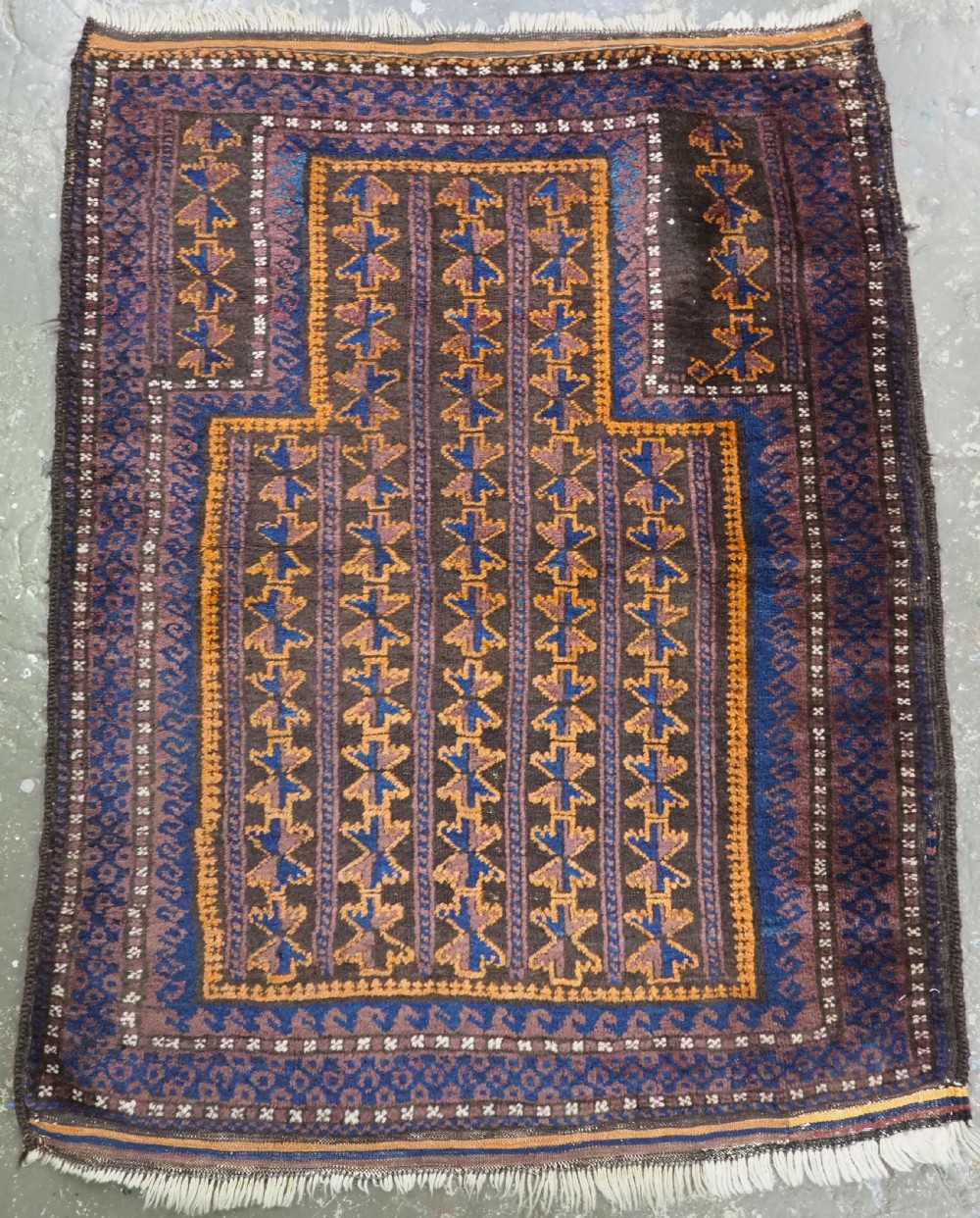 A hand-knotted antique Afghan Baluch wool prayer rug featuring a central arched mihrab design with repeating geometric motifs in brown, blue, and ochre.