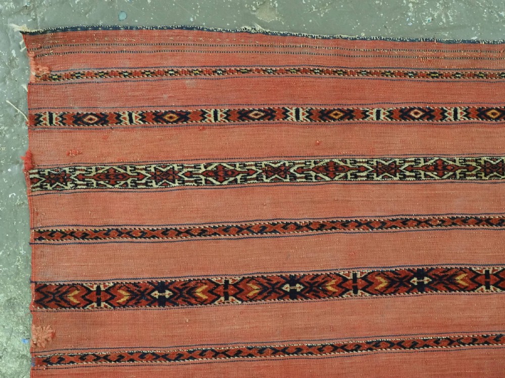 An antique Turkmen woven chuval face featuring horizontal bands of terracotta red and narrow geometric patterns in dark blue, black, and white with a fringed bottom edge. View II