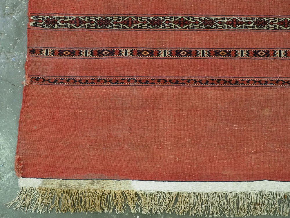 An antique Turkmen woven chuval face featuring horizontal bands of terracotta red and narrow geometric patterns in dark blue, black, and white with a fringed bottom edge. View III