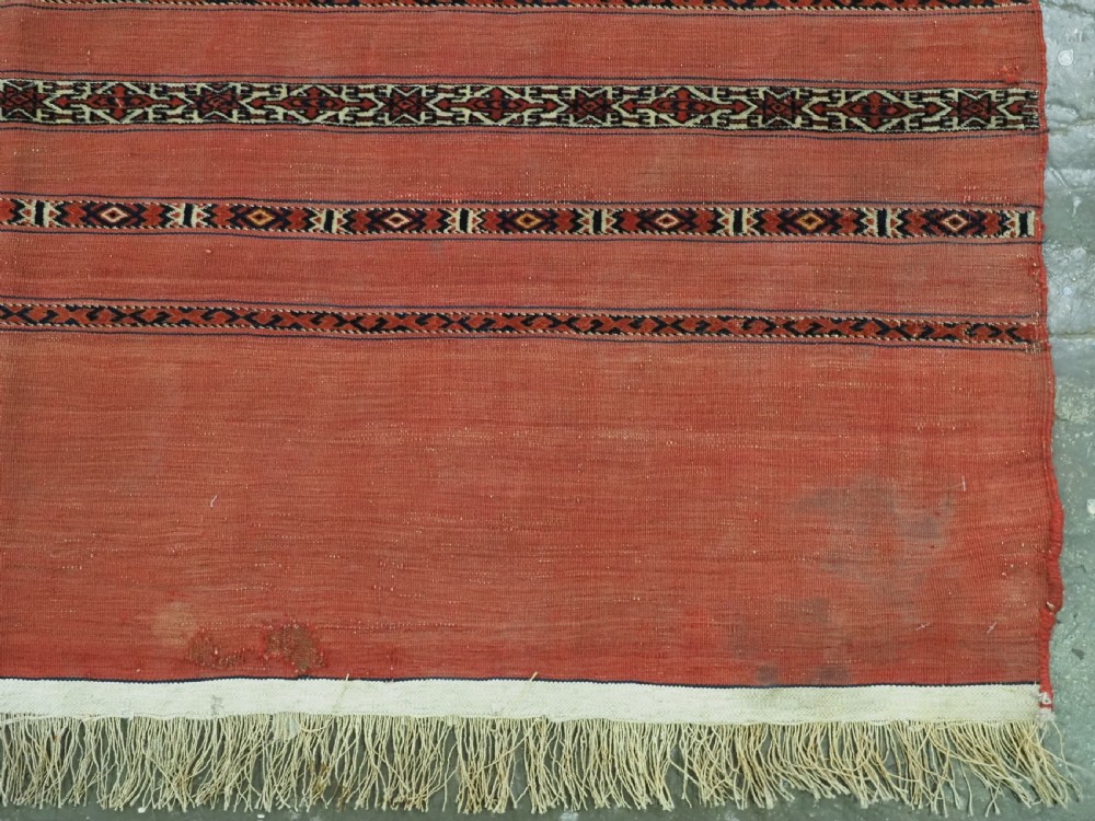 An antique Turkmen woven chuval face featuring horizontal bands of terracotta red and narrow geometric patterns in dark blue, black, and white with a fringed bottom edge. View V