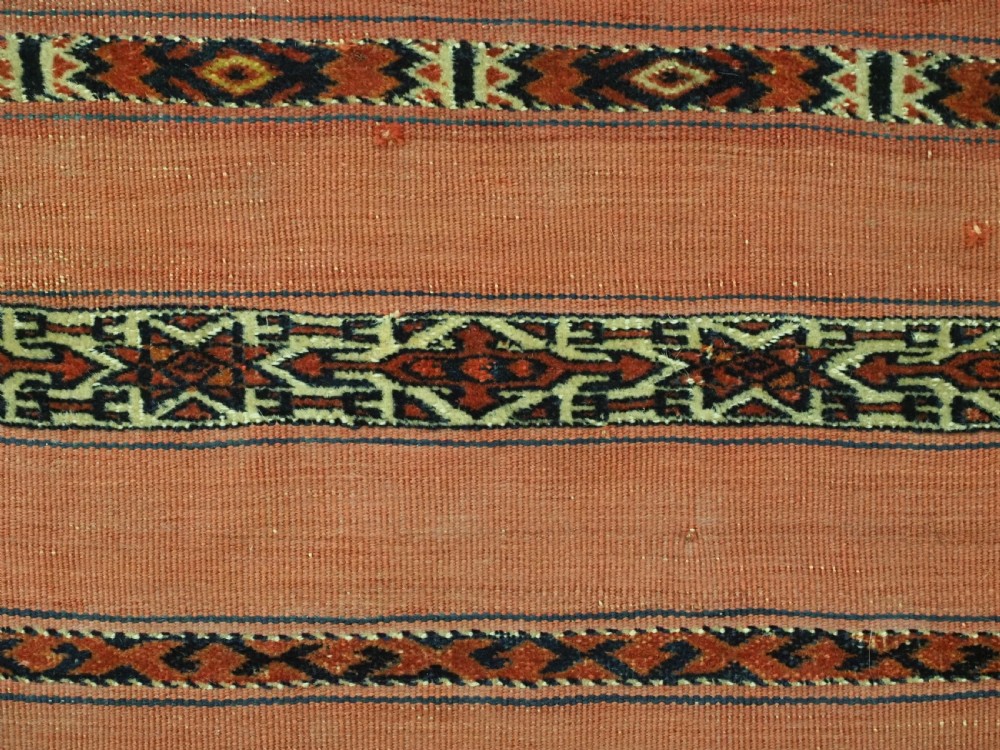 An antique Turkmen woven chuval face featuring horizontal bands of terracotta red and narrow geometric patterns in dark blue, black, and white with a fringed bottom edge. View VI