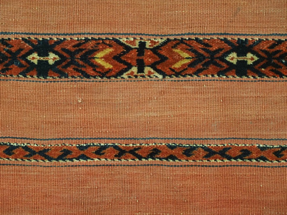 An antique Turkmen woven chuval face featuring horizontal bands of terracotta red and narrow geometric patterns in dark blue, black, and white with a fringed bottom edge. View VII