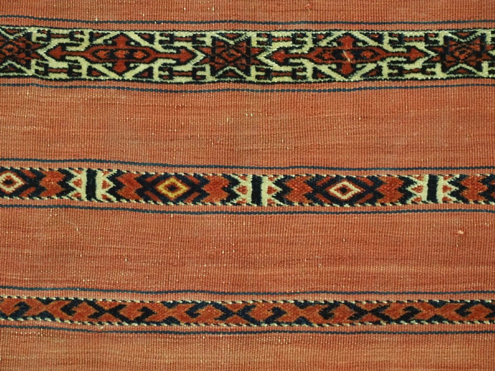An antique Turkmen woven chuval face featuring horizontal bands of terracotta red and narrow geometric patterns in dark blue, black, and white with a fringed bottom edge. View VIII