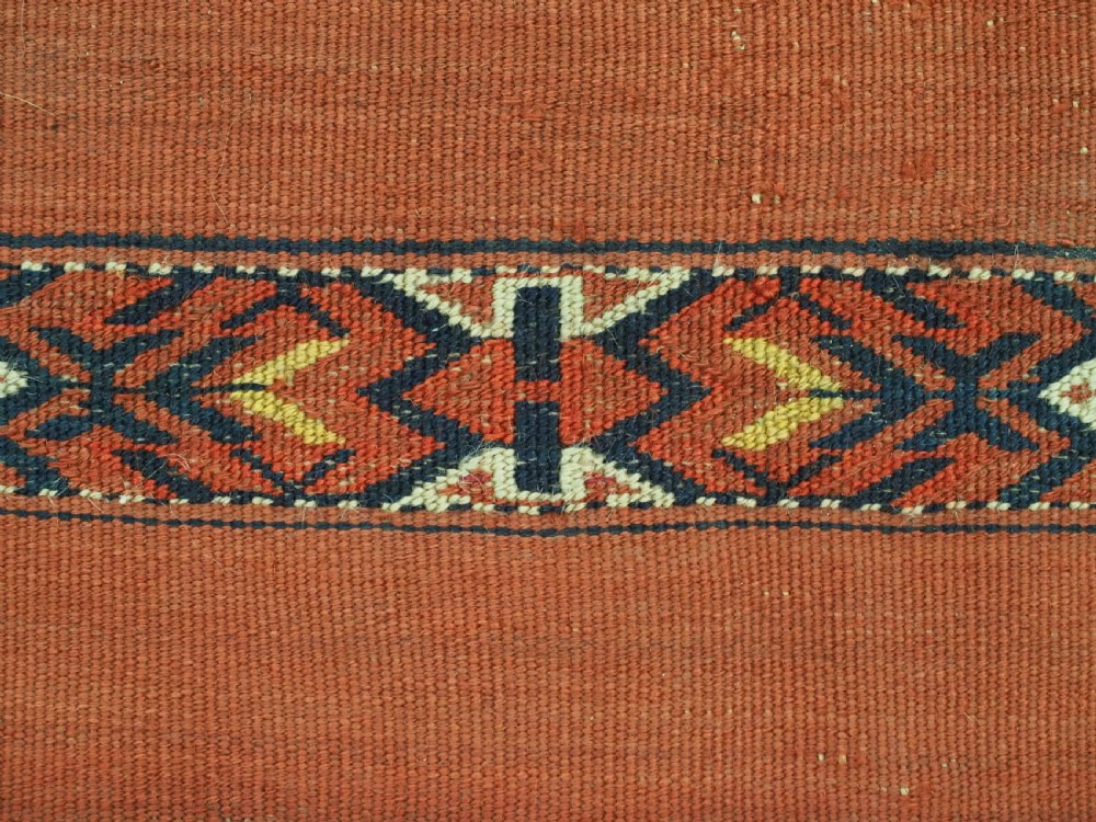 An antique Turkmen woven chuval face featuring horizontal bands of terracotta red and narrow geometric patterns in dark blue, black, and white with a fringed bottom edge. View IX