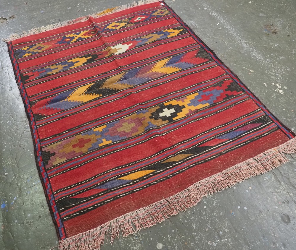 An antique flatweave Baluch kilim rug featuring horizontal red bands interspaced with colourful chevron and geometric motifs. View II
