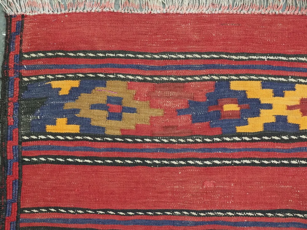 An antique flatweave Baluch kilim rug featuring horizontal red bands interspaced with colourful chevron and geometric motifs. View VI