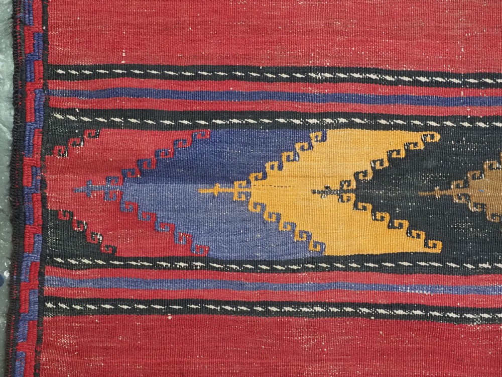 An antique flatweave Baluch kilim rug featuring horizontal red bands interspaced with colourful chevron and geometric motifs. View VII