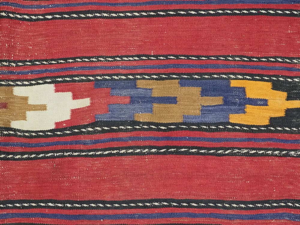 An antique flatweave Baluch kilim rug featuring horizontal red bands interspaced with colourful chevron and geometric motifs. View VIII