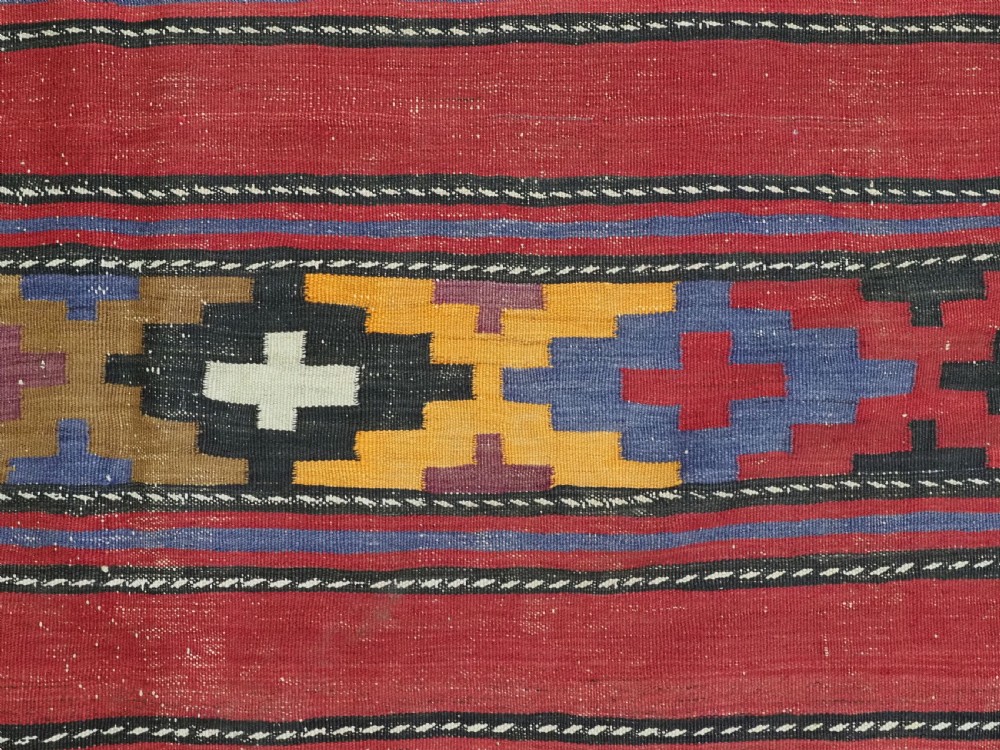 An antique flatweave Baluch kilim rug featuring horizontal red bands interspaced with colourful chevron and geometric motifs. View IX