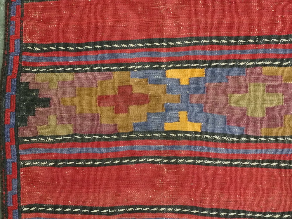 An antique flatweave Baluch kilim rug featuring horizontal red bands interspaced with colourful chevron and geometric motifs. View X
