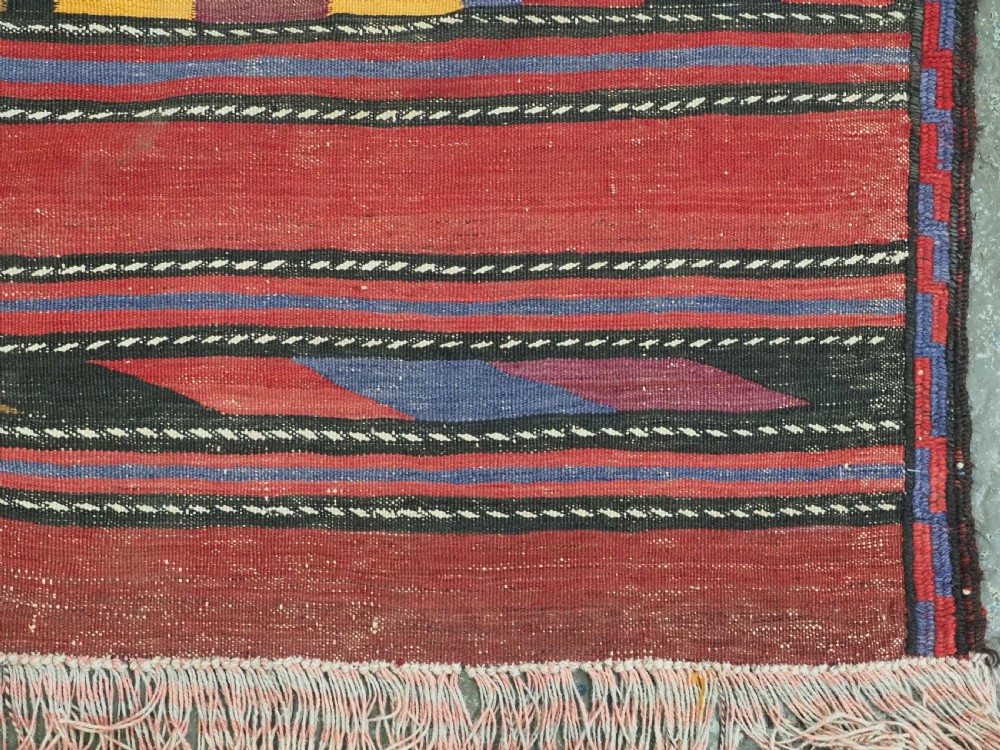 An antique flatweave Baluch kilim rug featuring horizontal red bands interspaced with colourful chevron and geometric motifs. View XI