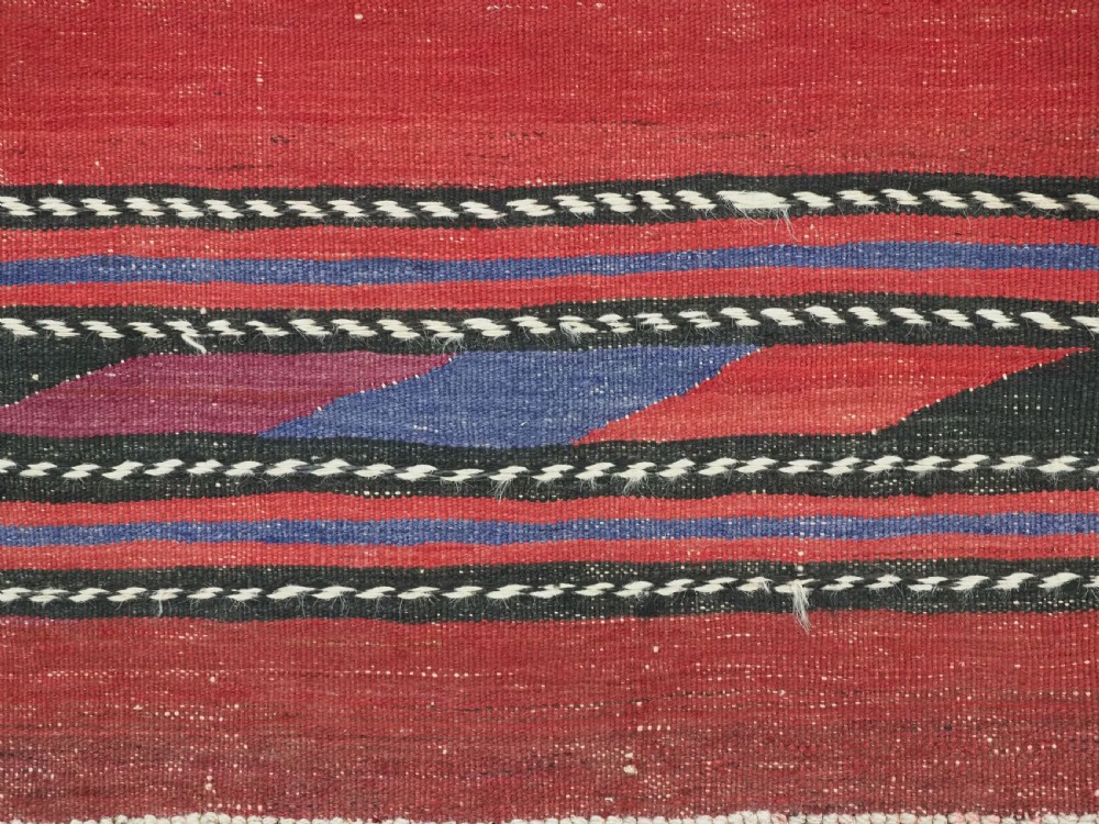 An antique flatweave Baluch kilim rug featuring horizontal red bands interspaced with colourful chevron and geometric motifs. View XII