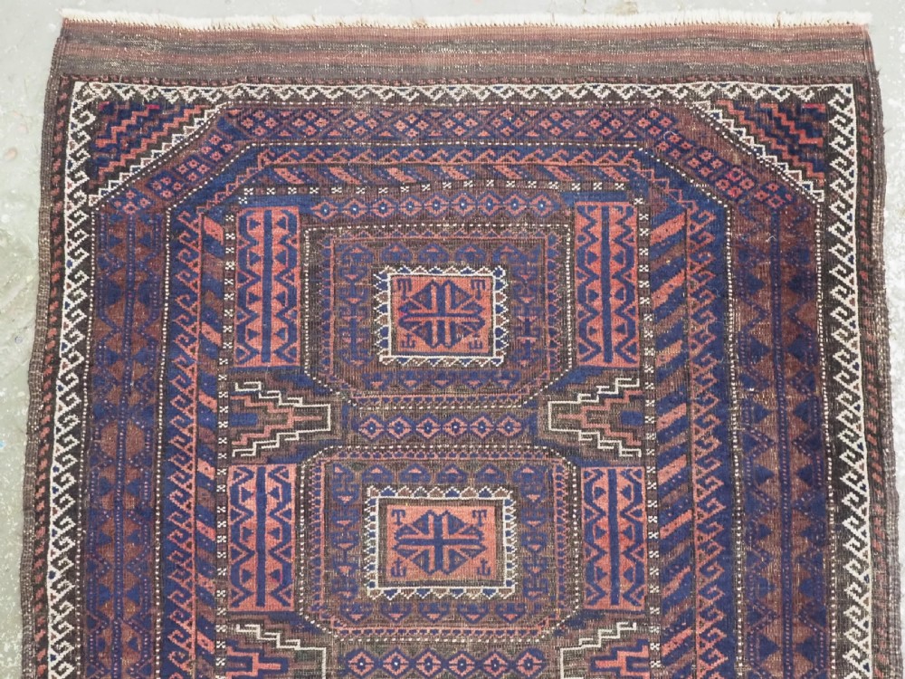 An antique rectangular Baluch tribal rug featuring five central geometric box medallions in dark red and indigo blue against a patterned ground. View III